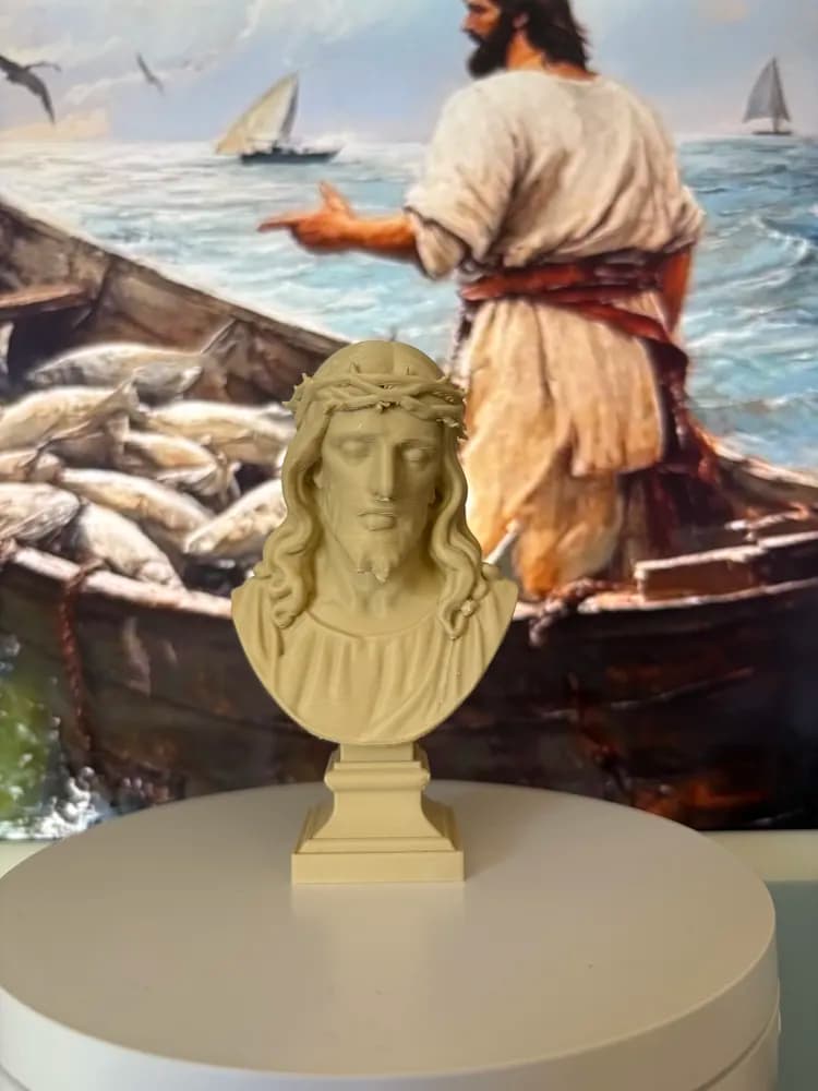 Busto artesanal de Cristo em pedestal sobre mesa, ao fundo quadro religioso de Jesus no mar