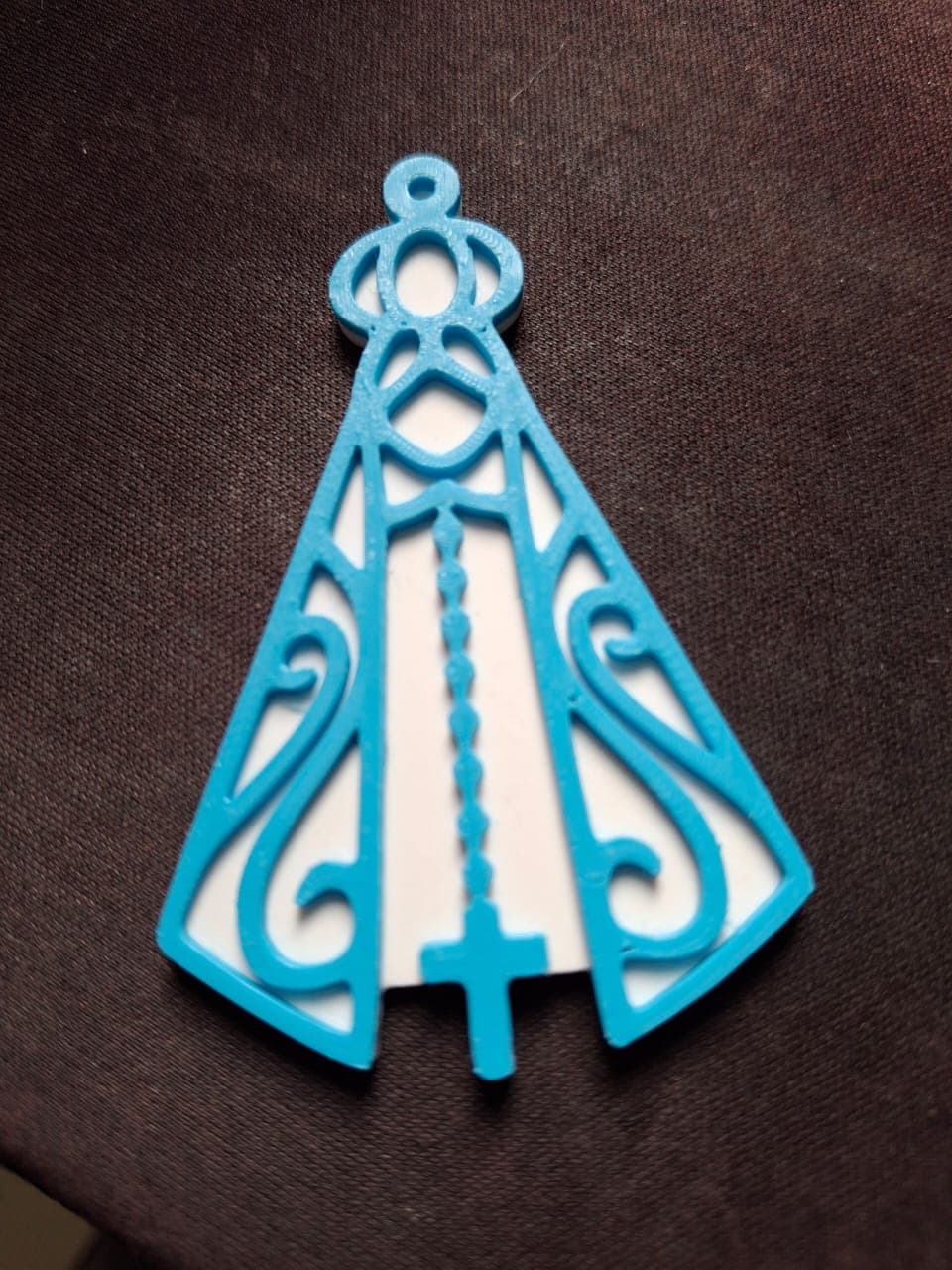 Chaveiro de Nossa Senhora Aparecida sobre tecido escuro, mostrando os detalhes do manto rendado e a cruz na base