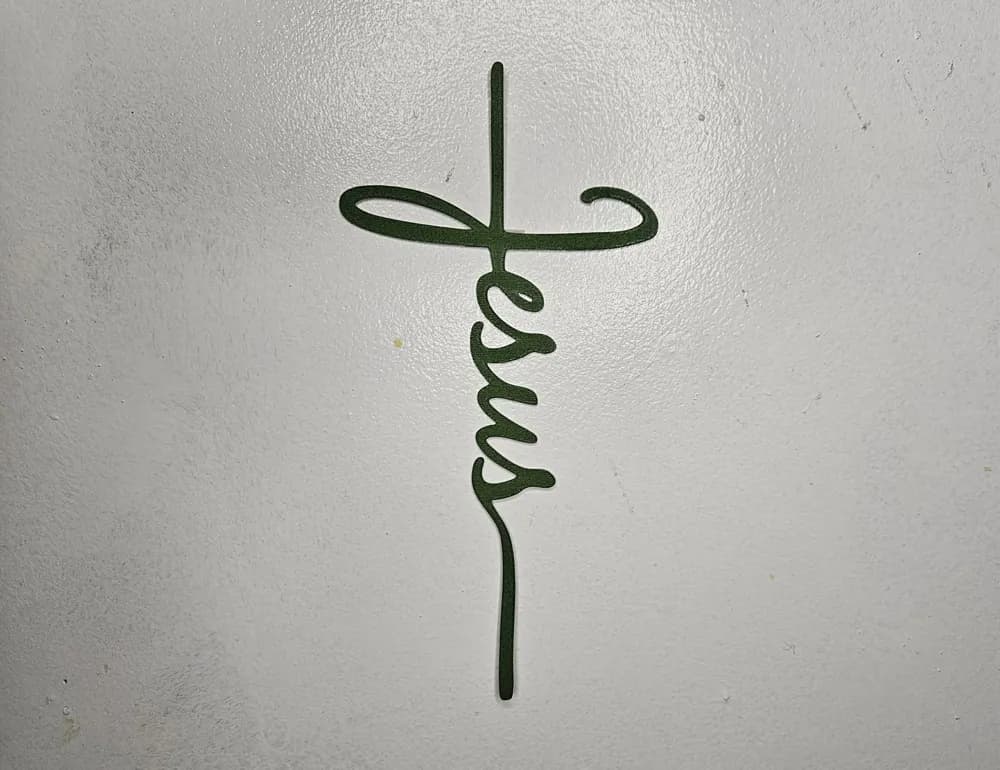 Cruz Jesus cursivo vista frontal em parede branca mostrando o traçado fino do recorte