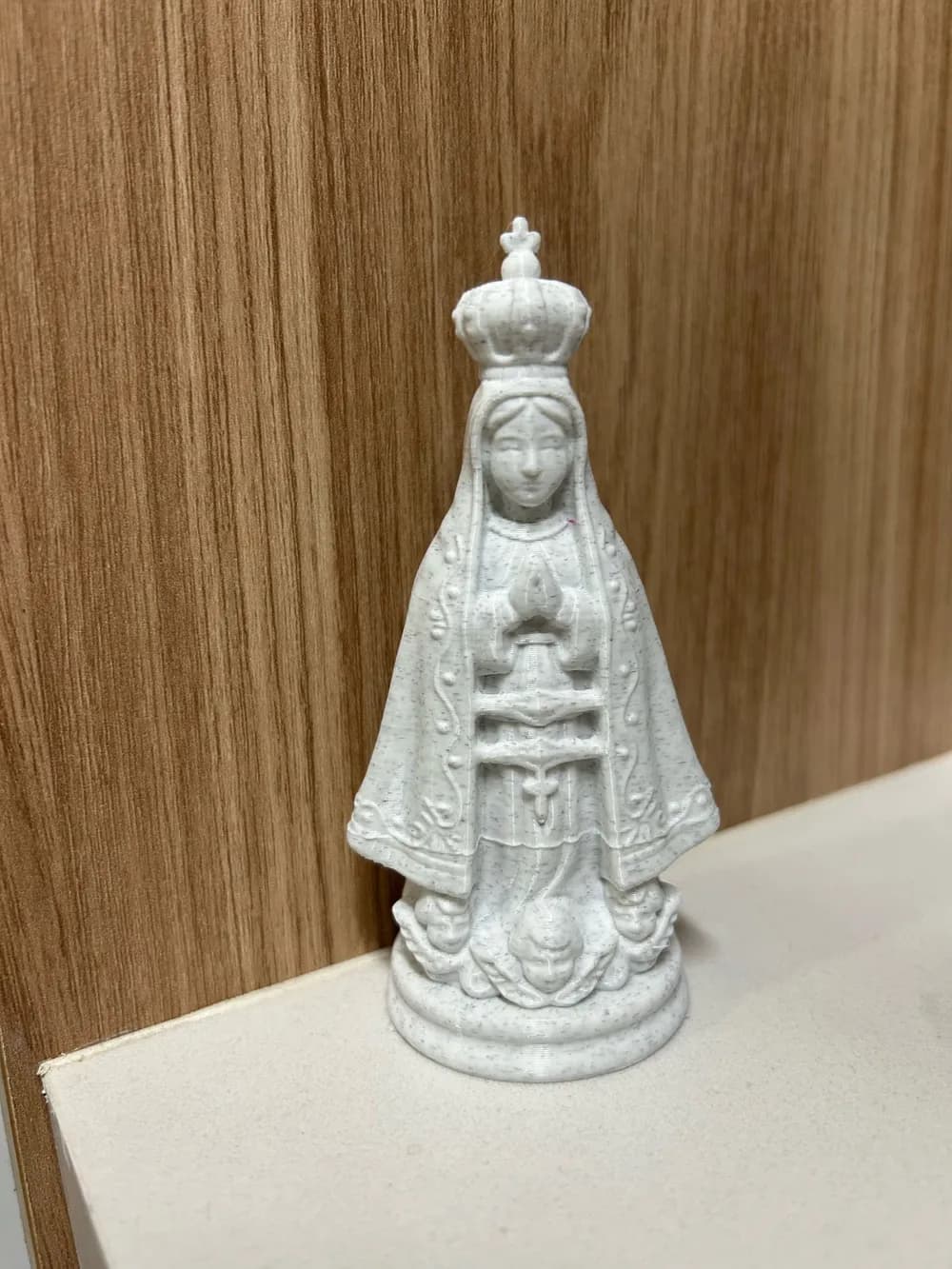 Nossa Senhora Aparecida Orante em acabamento perolado, manto com relevos e coroa, sobre prateleira branca com parede de madeira