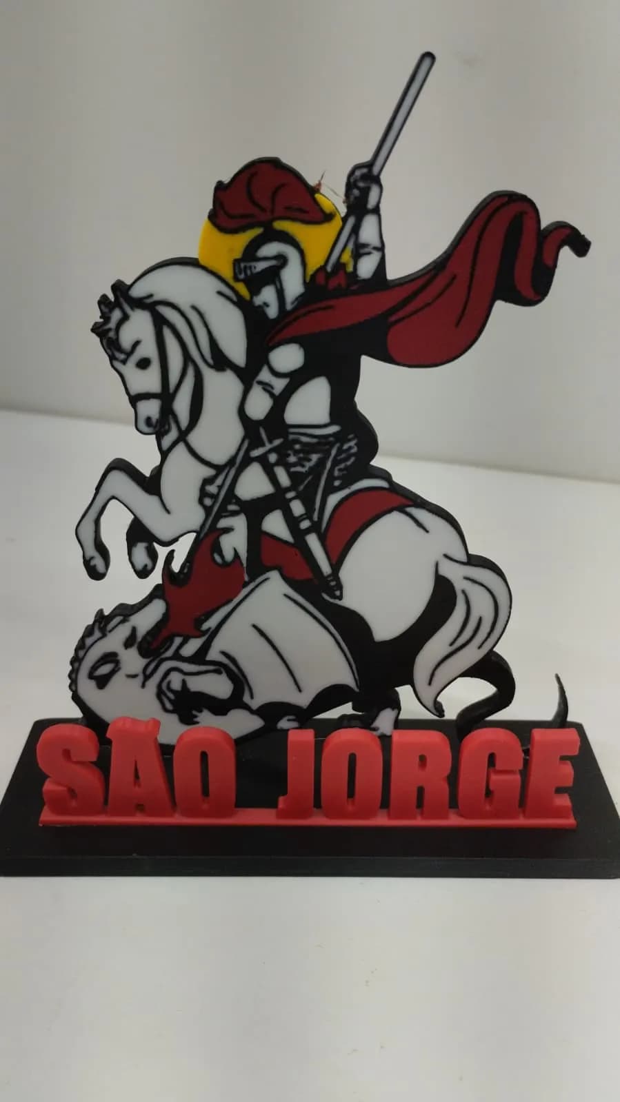 Vista frontal da peça de São Jorge, mostrando o cavaleiro com armadura, capa vermelha e auréola dourada sobre o dragão