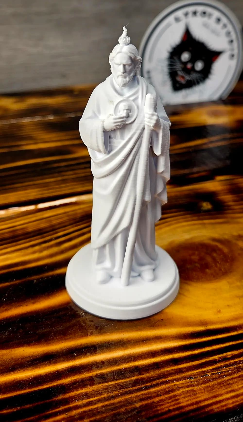 Escultura artesanal de São Judas Tadeu sobre superfície de madeira, detalhes do hábito e da expressão serena